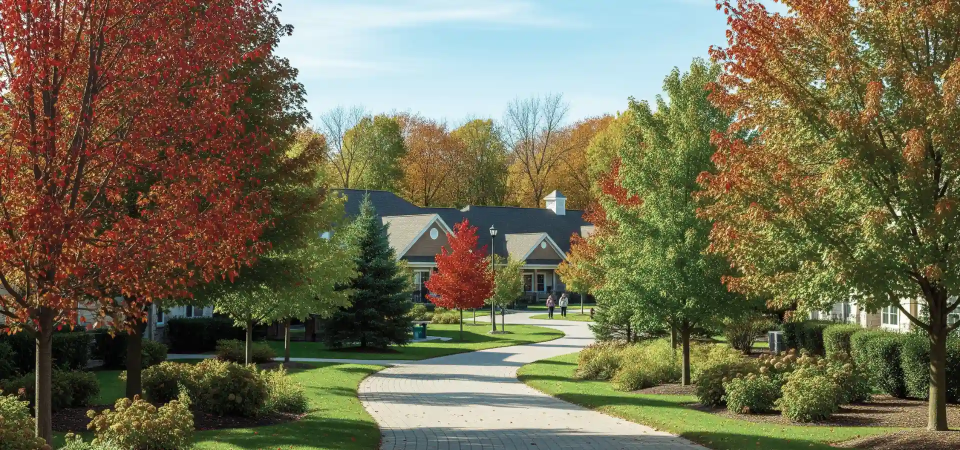 A curved path through a senior living campus surrounded by autumn trees and landscaped gardens.